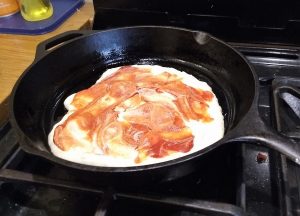 Rolled out dough in skillet with cashew cream and tomato paste spread on it
